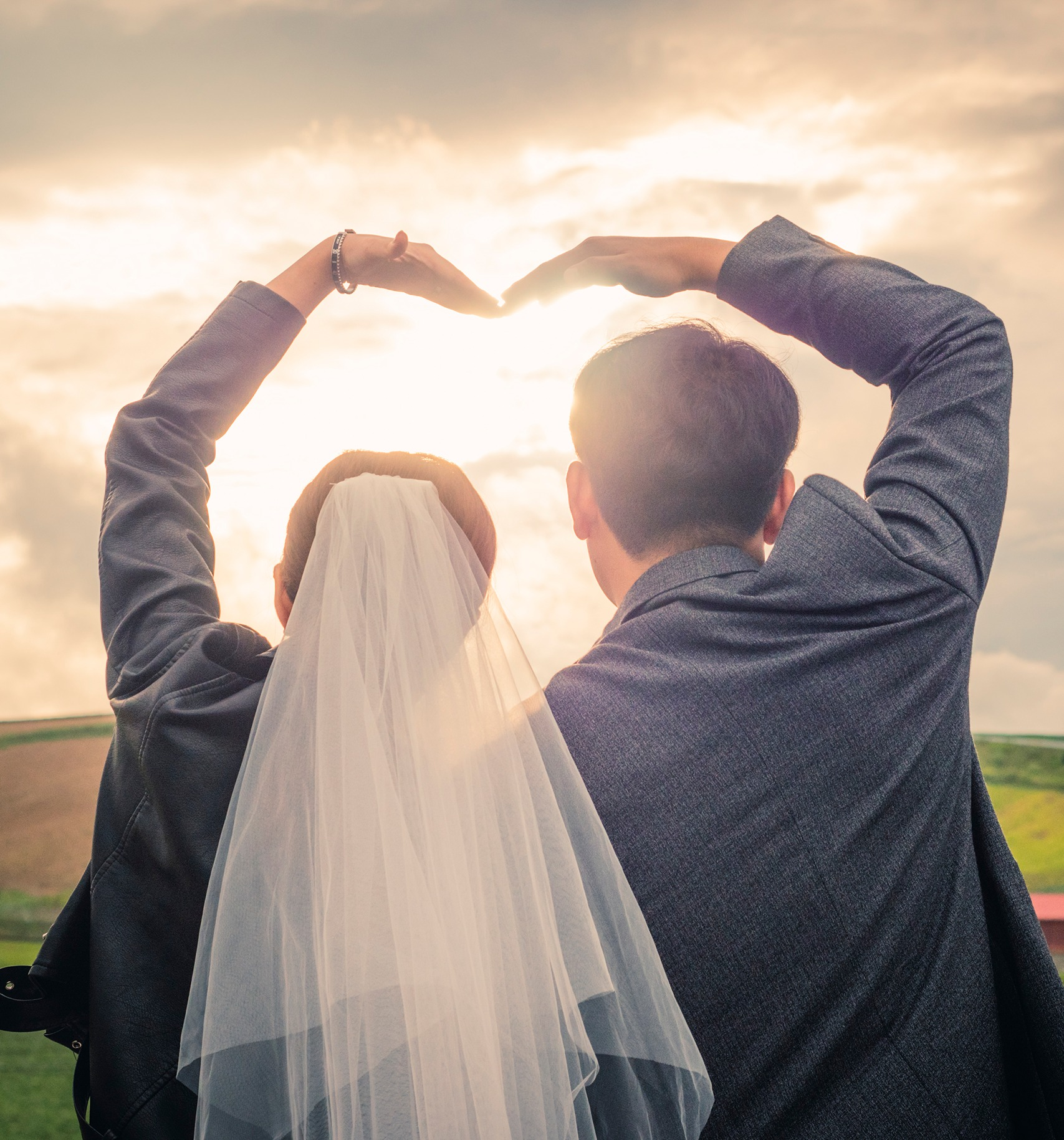 bride and groom forming a heart shape with heart hands over their heads